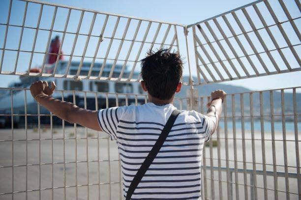 Boy stands at a fence looking at a port